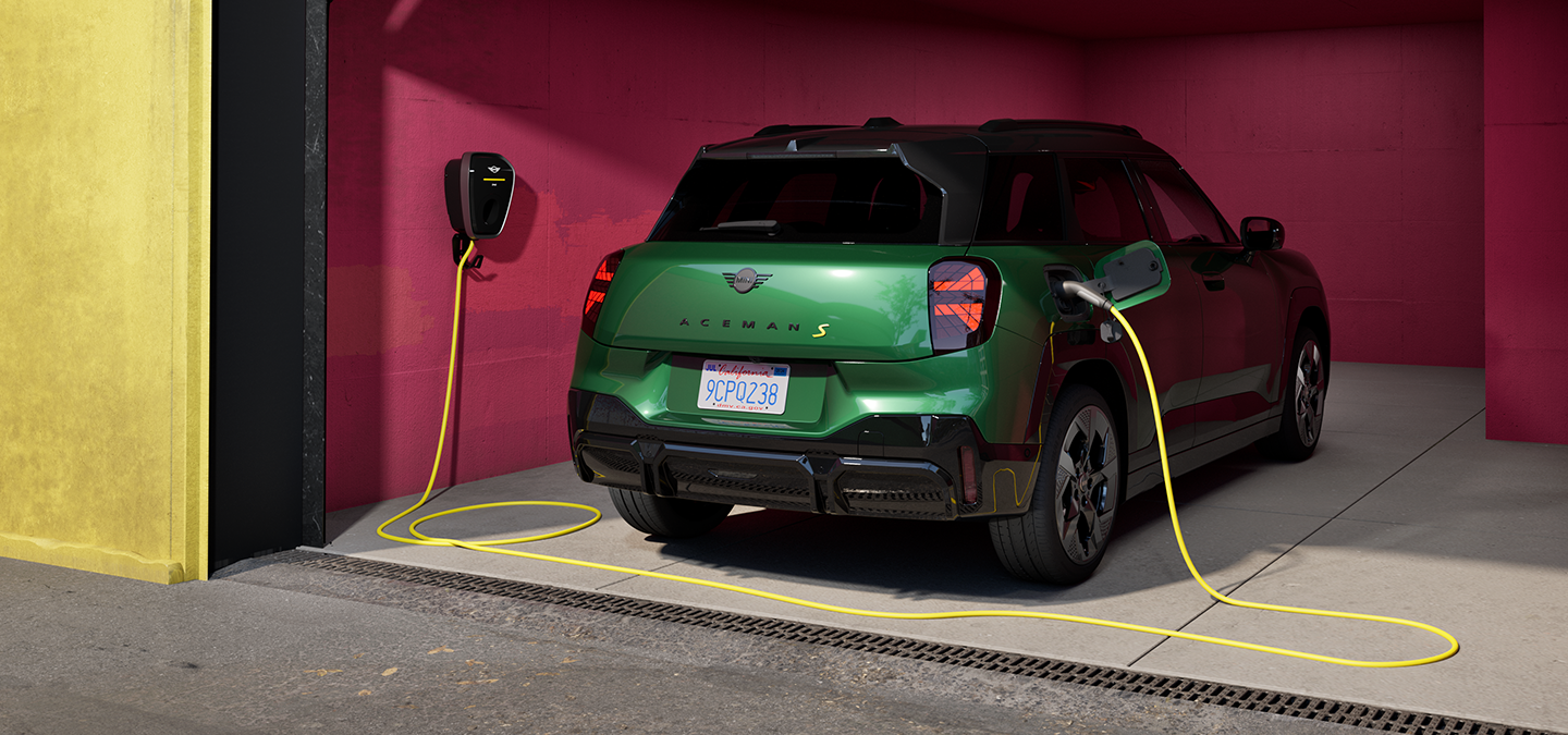 Πίσω όψη του αμιγώς ηλεκτρικού MINI Aceman σε χρώμα British Racing Green να φορτίζει σε γκαράζ. 