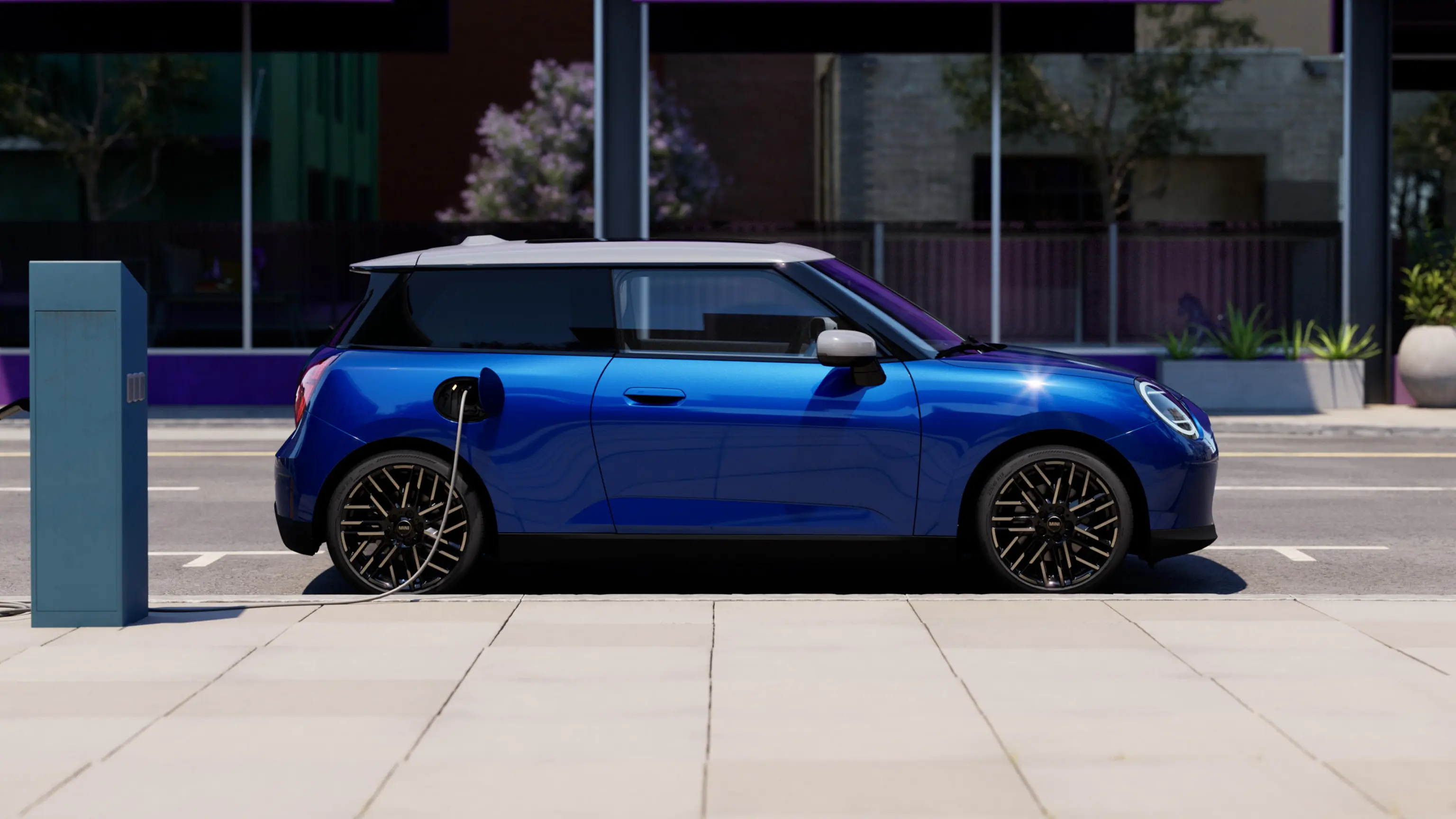 Πλαϊνή όψη αμιγώς ηλεκτρικού MINI Cooper σε Blazing Blue σταθμευμένο σε πεζοδρόμιο δίπλα σε σταθμό φόρτισης