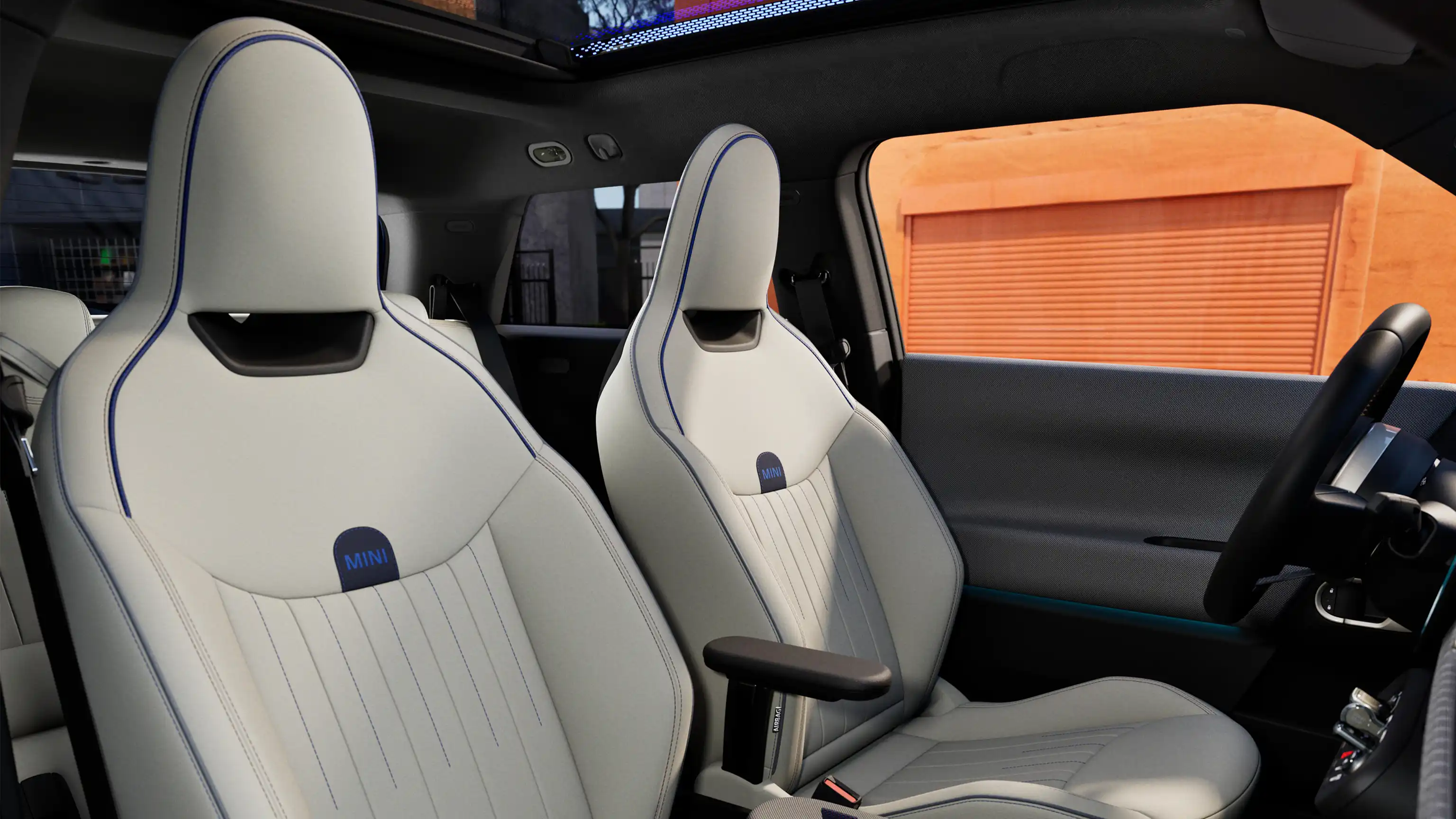 Εσωτερική άποψη του αμιγώς ηλεκτρικού MINI Cooper, διακρίνεται το ταμπλό, το τιμόνι, η κυκλική οθόνη, η πανοραμική γυάλινη οροφή και το πίσω μέρος των μπροστινών καθισμάτων