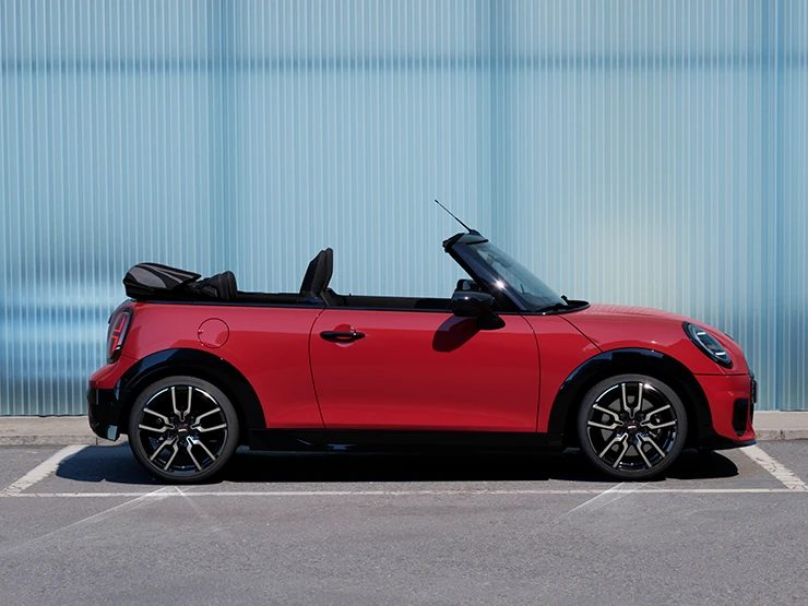 Πλάγια όψη του MINI Cooper Cabrio σε χρώμα Chili Red σε δρόμο.