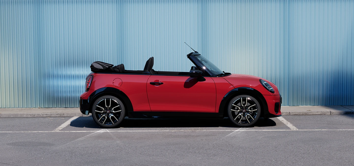 Πλάγια όψη του MINI Cooper Cabrio σε χρώμα Chili Red σε δρόμο.
