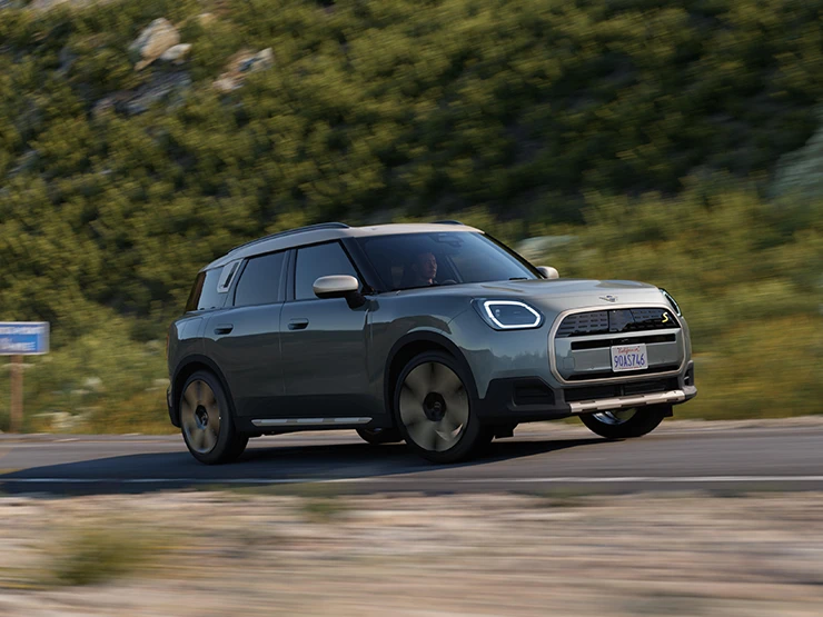 Πλευρική όψη του αμιγώς ηλεκτρικού MINI Countryman σε χρώμα Smokey Green και οροφή σε χρώμα Vibrant Silver, κινούμενο εκτός δρόμου.