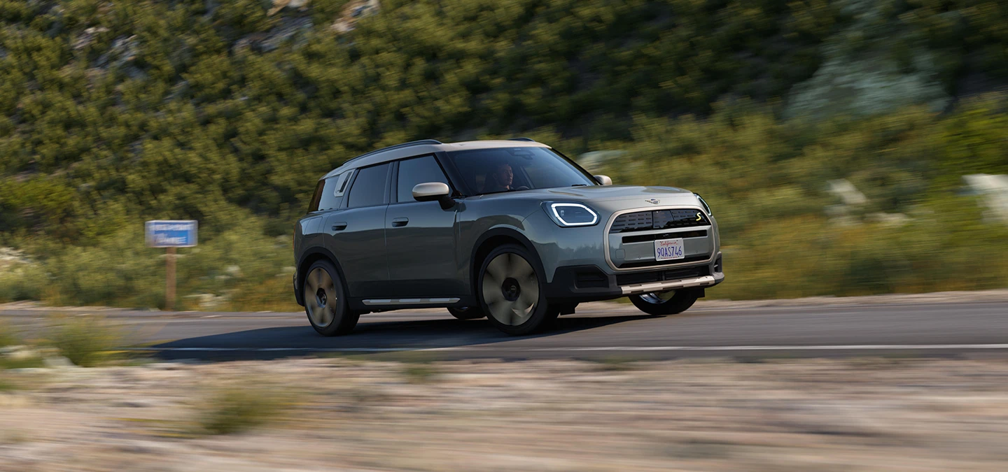 Πλευρική όψη του αμιγώς ηλεκτρικού MINI Countryman σε χρώμα Smokey Green και οροφή σε χρώμα Vibrant Silver, κινούμενο εκτός δρόμου.