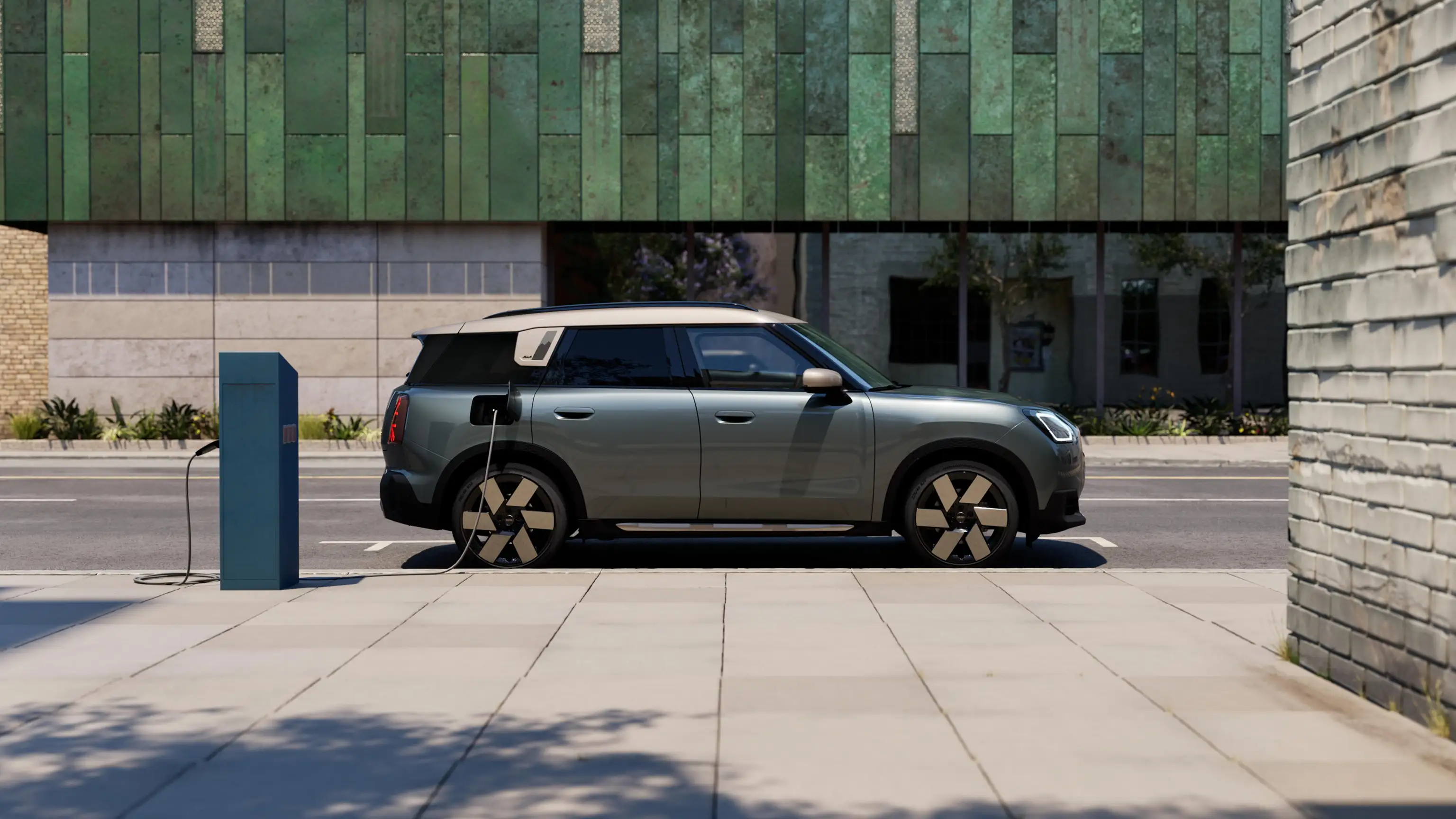 Πλάγια όψη ενός αμιγώς ηλεκτρικού MINI Countryman σε Smokey Green με οροφή Vibrant Silver που φορτίζεται στον δρόμο