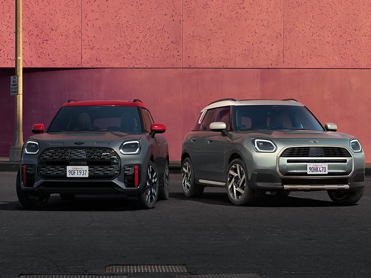 Μπροστινή όψη του MINI Countryman JCW σε χρώμα Legend Grey και κόκκινη οροφή και του MINI Countryman σε χρώμα Smokey Green και οροφή σε χρώμα Vibrant Silver να στέκονται το ένα δίπλα στο άλλο.