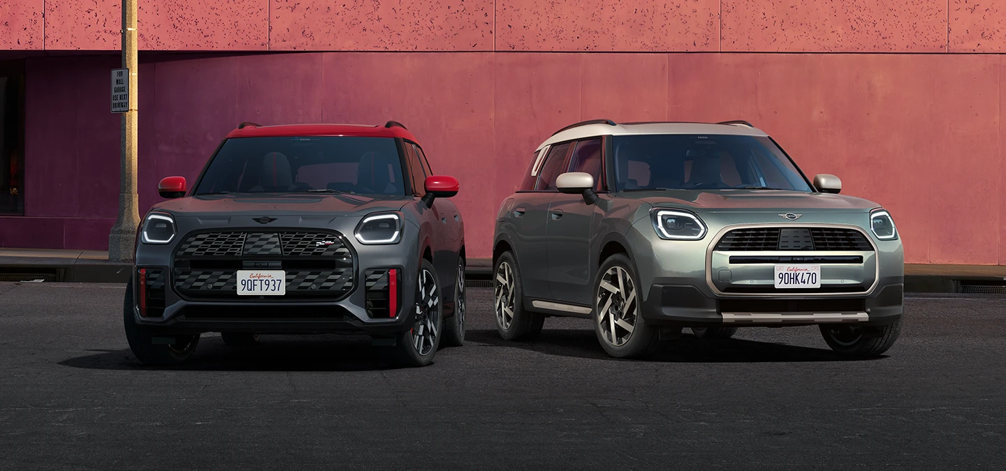 Μπροστινή όψη του MINI Countryman JCW σε χρώμα Legend Grey και κόκκινη οροφή και του MINI Countryman σε χρώμα Smokey Green και οροφή σε χρώμα Vibrant Silver να στέκονται το ένα δίπλα στο άλλο.