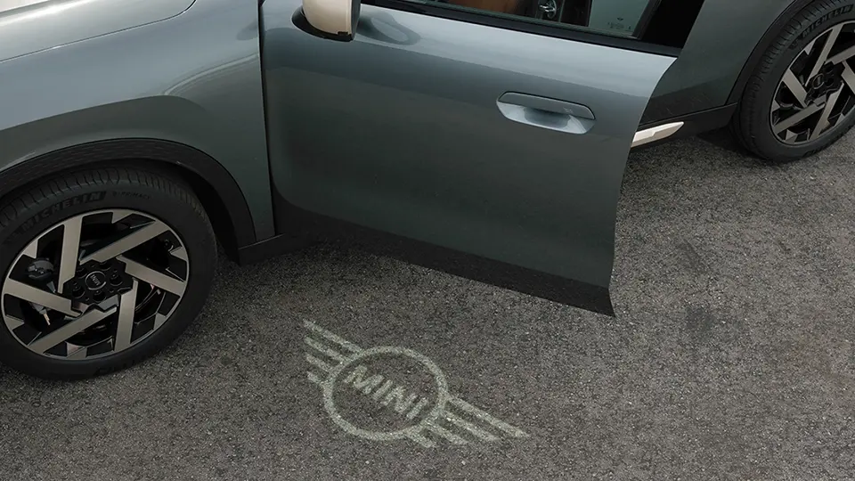 Εξωτερική όψη MINI Countryman με ανοιχτή πόρτα και φωτισμό καλωσορίσματος στο έδαφος με λογότυπο MINI