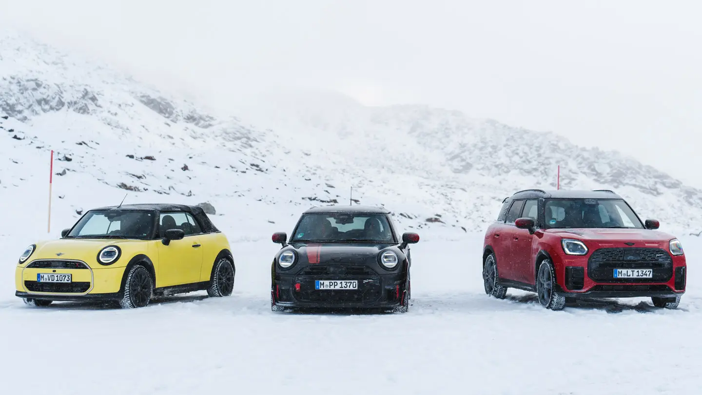 MINI Cooper Cabrio σε Sunny Side Yellow, MINI John Cooper Works σε Midnight Black II και MINI Countryman Cooper σε Chilli Red – σταθμευμένα σε χιονισμένο ορεινό δρόμο, μπροστινή όψη.