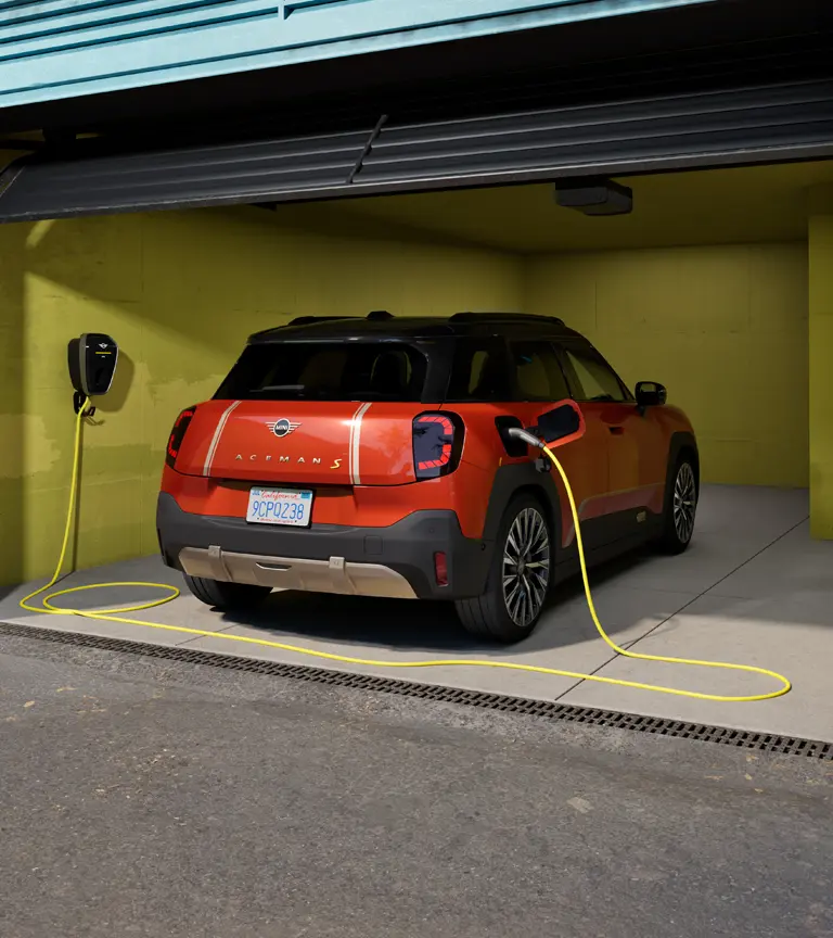 Αμιγώς ηλεκτρικό MINI Aceman S φορτίζει σε MINI Wallbox Plus, πίσω όψη, σταθμευμένο σε γκαράζ.