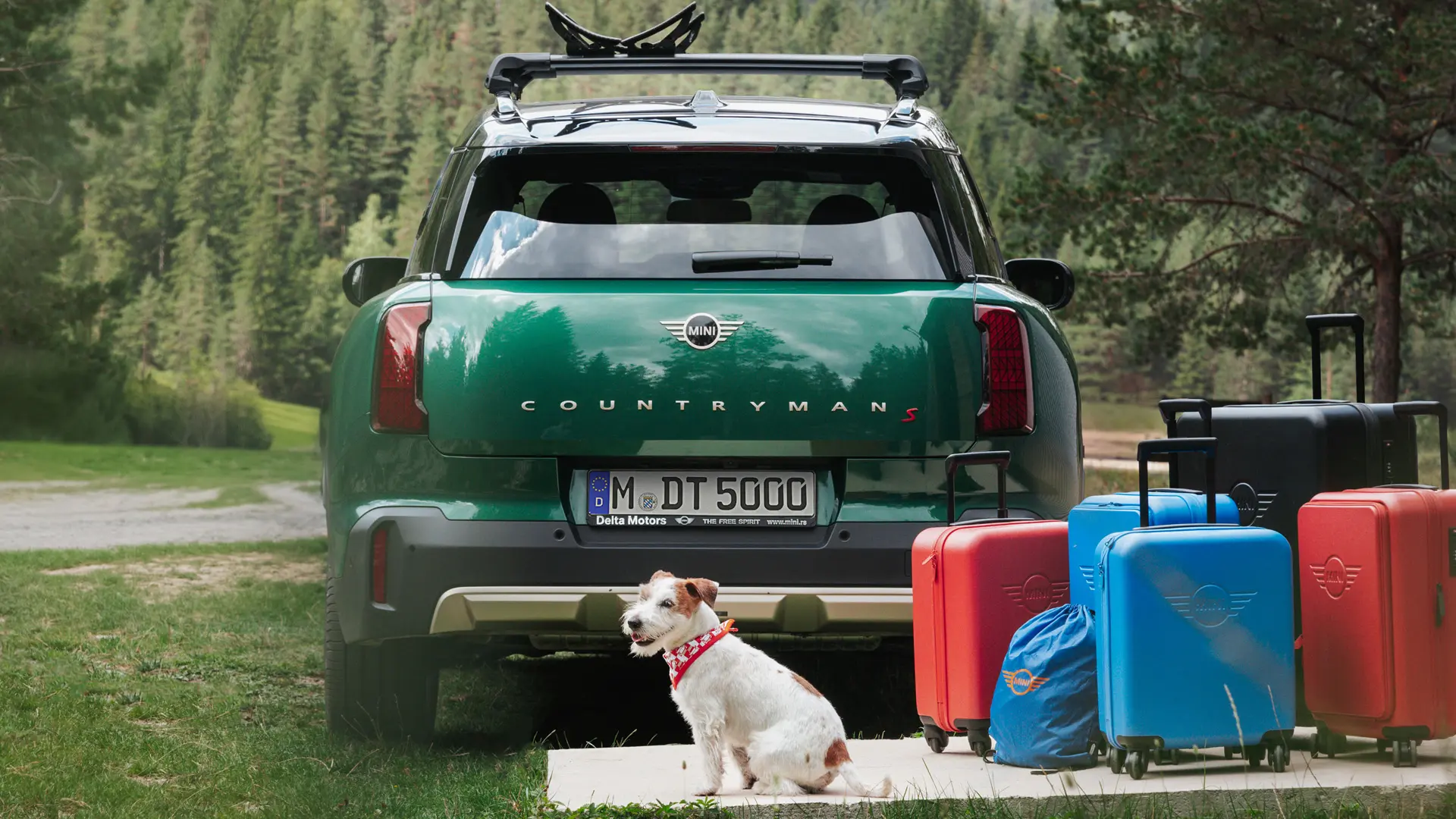 MINI Countryman σε πράσινο χρώμα, πίσω από το αυτοκίνητο υπάρχουν διάφορες αποσκευές που διατίθενται από το MINI Lifestyle καθώς κι ένας σκύλος ράτσας Jack Russell. 