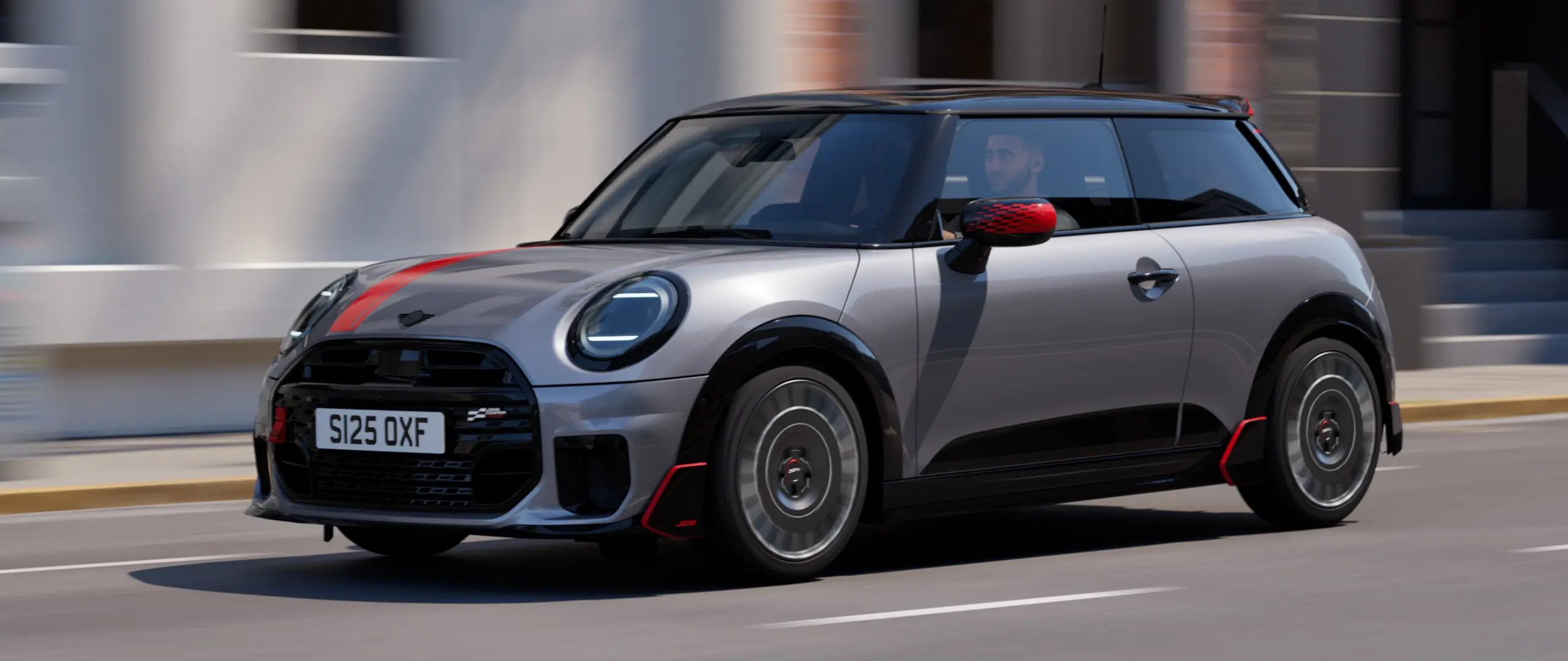 Ένα 3-θυρο MINI Cooper σε Melting Silver με καλύμματα εξωτερικών καθρεπτών John Cooper Works και αυτοκόλλητο στο καπό του κινητήρα σε Chili Red, αεροτομή οροφής και πτερύγια αεροτομής σε μαύρο χρώμα κινείται σε έναν αστικό δρόμο – μπροστινή όψη από το πλάι.