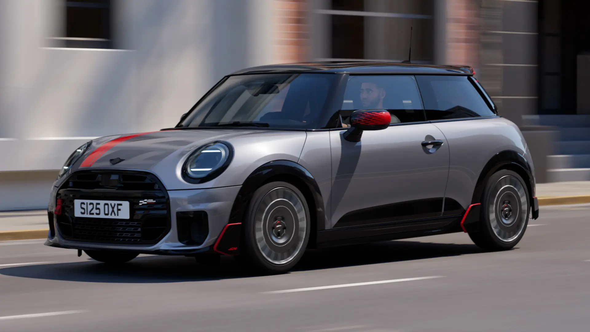 Ένα 3-θυρο MINI Cooper σε Melting Silver με καλύμματα εξωτερικών καθρεπτών John Cooper Works και αυτοκόλλητο στο καπό του κινητήρα σε Chili Red, αεροτομή οροφής και πτερύγια αεροτομής σε μαύρο χρώμα κινείται σε έναν αστικό δρόμο – μπροστινή όψη από το πλάι.
