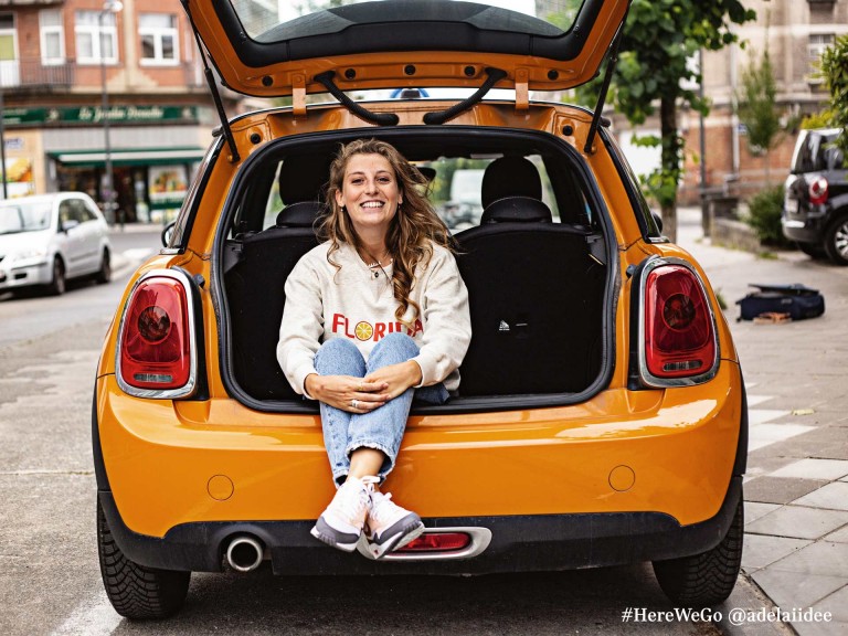 Τρίθυρο MINI Hatch σε volcanic orange με χαρούμενη γυναίκα να κάθεται στον χώρο αποσκευών